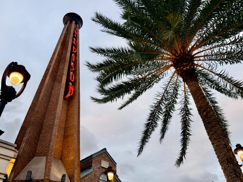 The Edison smokestack with its red neon sign beside a palm tree at Disney Springs