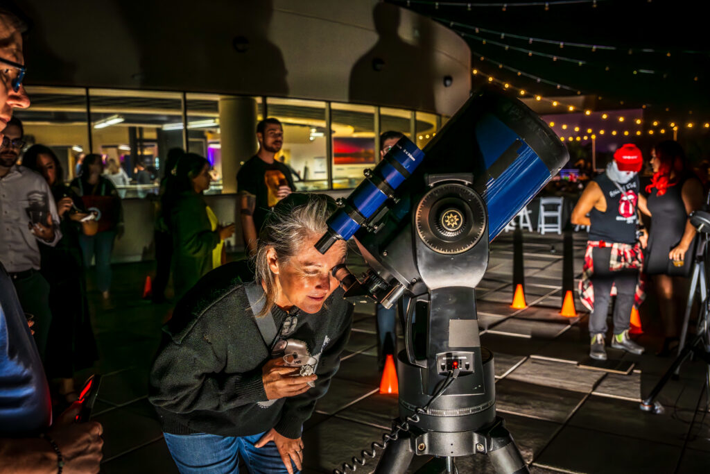 Guest looking through a telescope on the outdoor terrace at OSC After Dark, Orlando Science Center