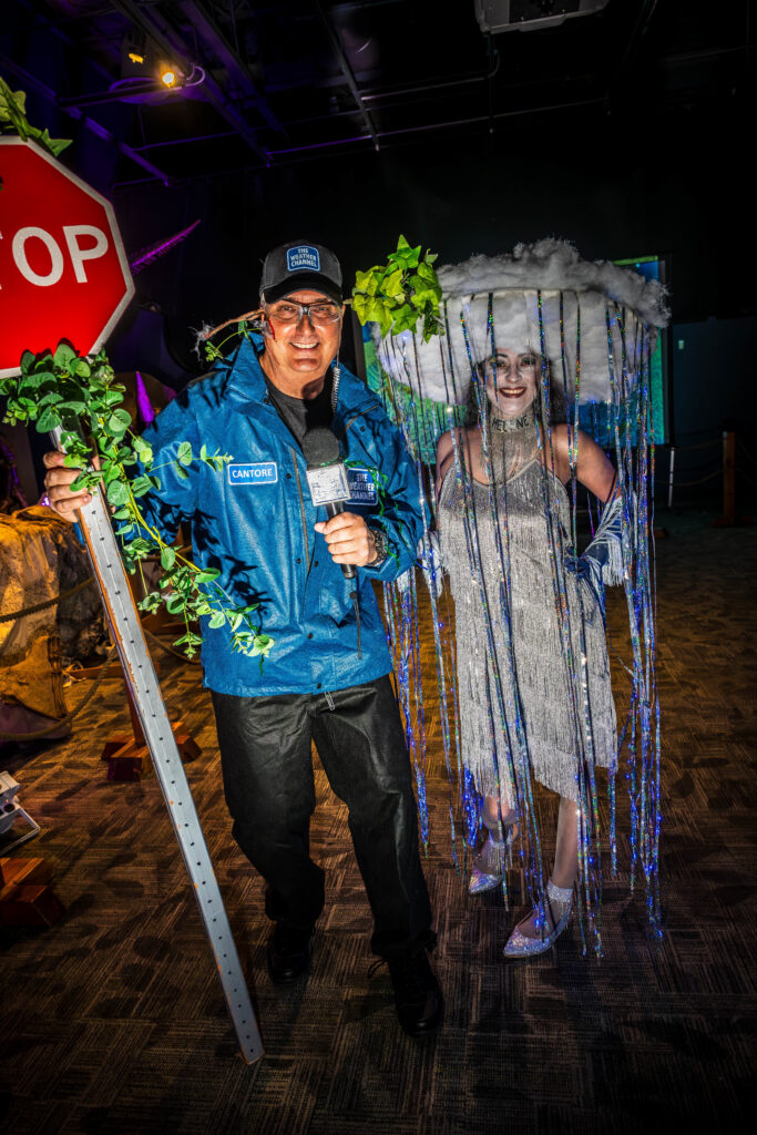 Guest in a rain cloud costume posing with a man holding a vine-covered stop sign at OSC After Dark, Orlando Science Center