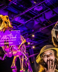 OSC After Dark 2026 guests in explorer costumes posing beneath a glowing dinosaur skeleton in DinoDigs at Orlando Science Center