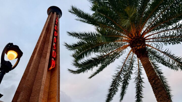 The Edison smokestack with its red neon sign beside a palm tree at Disney Springs