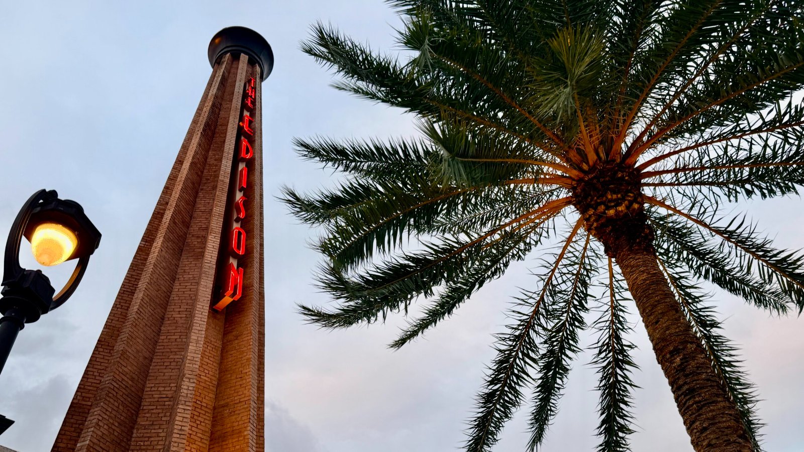 The Edison smokestack with its red neon sign beside a palm tree at Disney Springs
